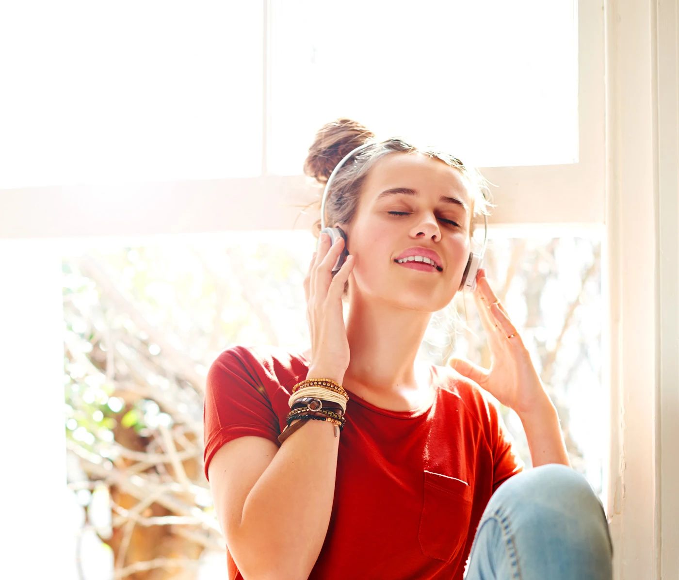 Woman wearing headphones near a sunlit window