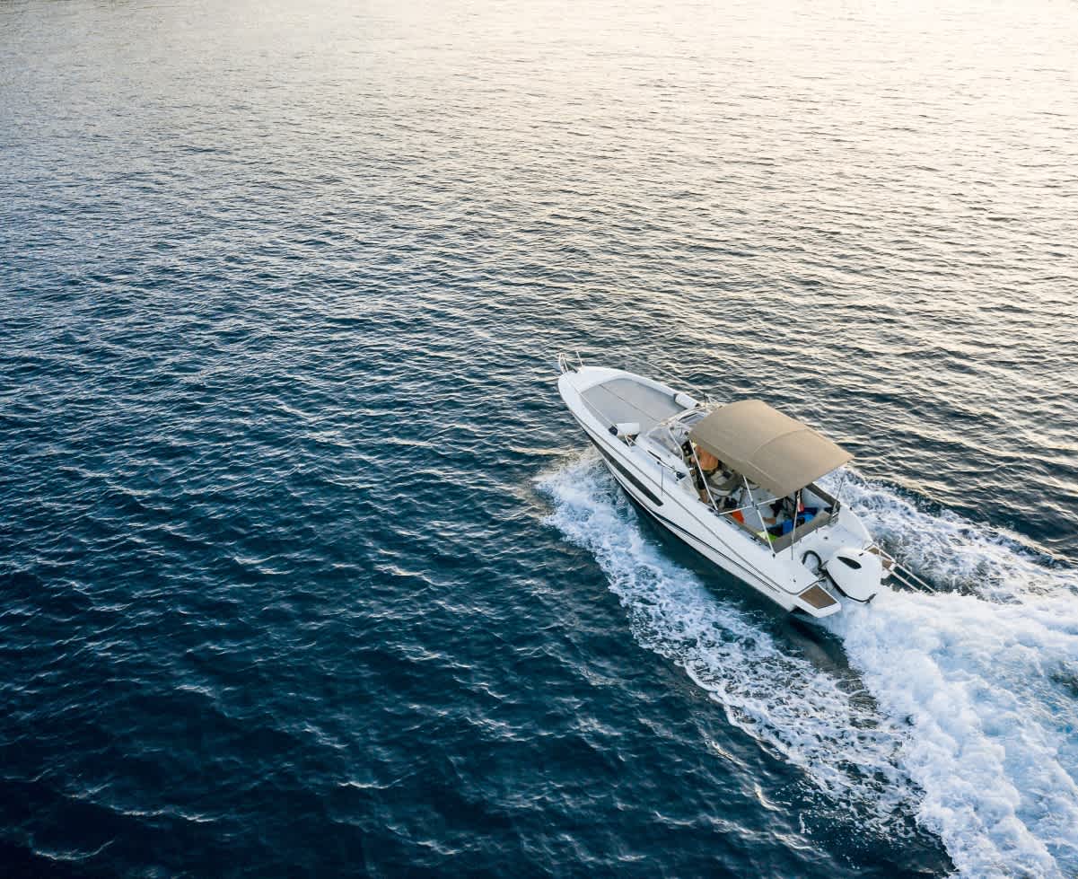 A bird's eye view of a white motorboat with a beige canopy cruising along choppy water.