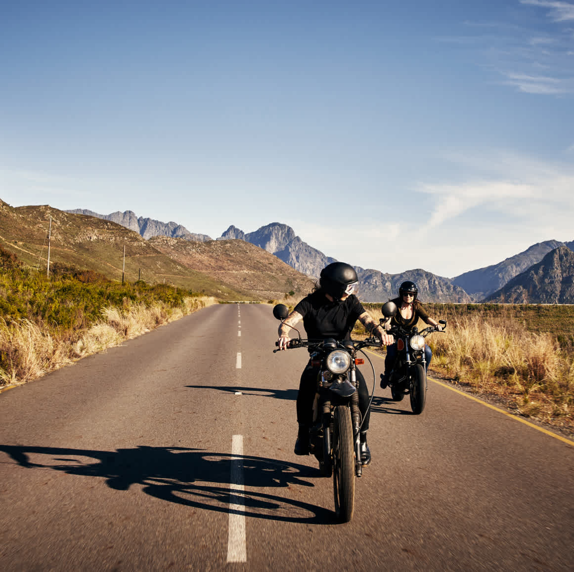 2 people on motorcycles driving on a road through mountains 