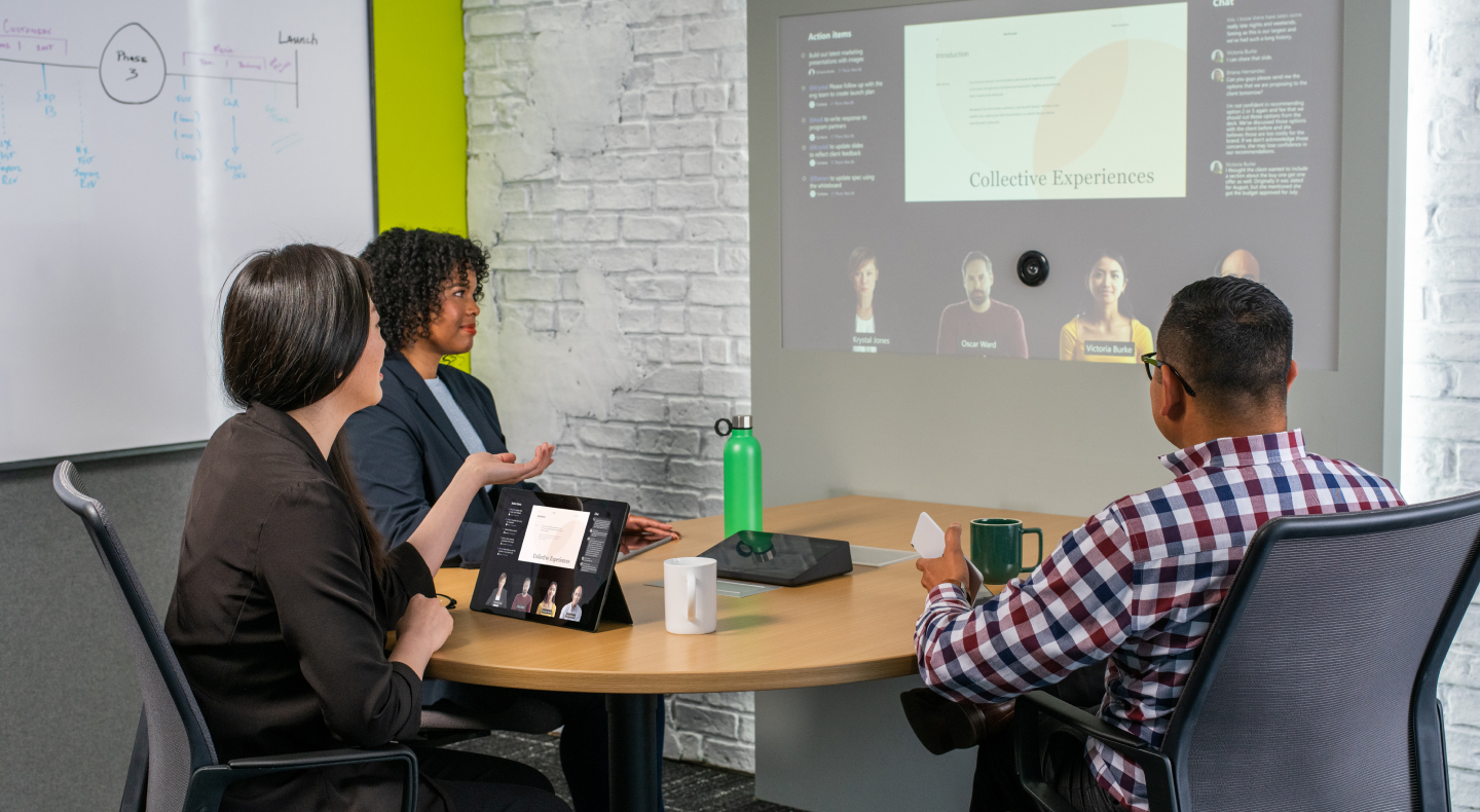 A photograph showing three people sitting around a table for a video call.