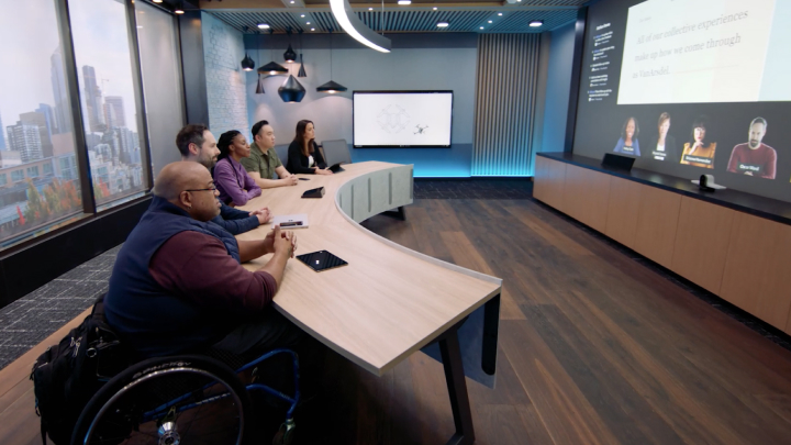 Several people sit at a desk in a redesigned Teams meeting room