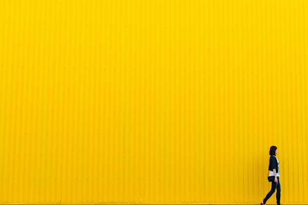 woman walking past a yellow wall