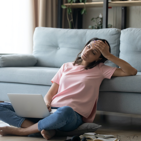 Woman holding her head, sitting on the floor.