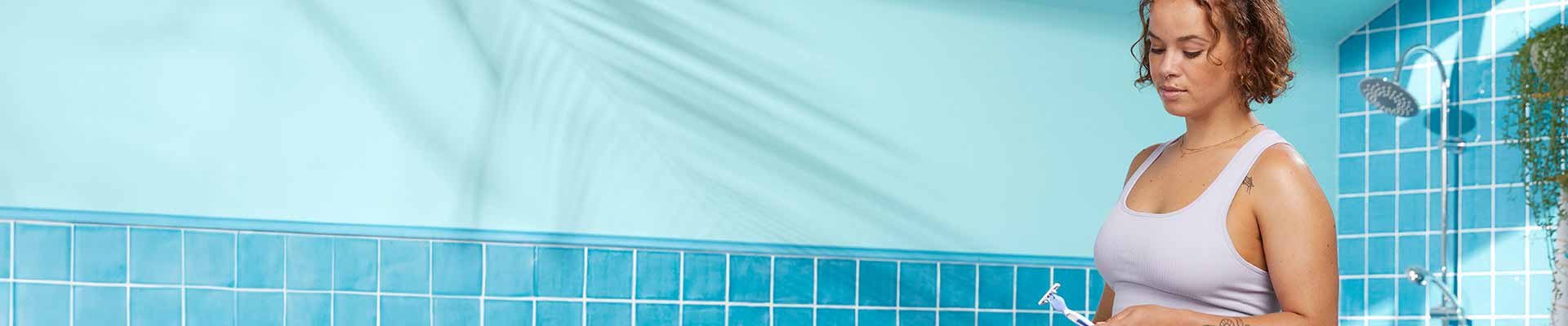 Jeune femme regardant un rasoir dans la salle de bain