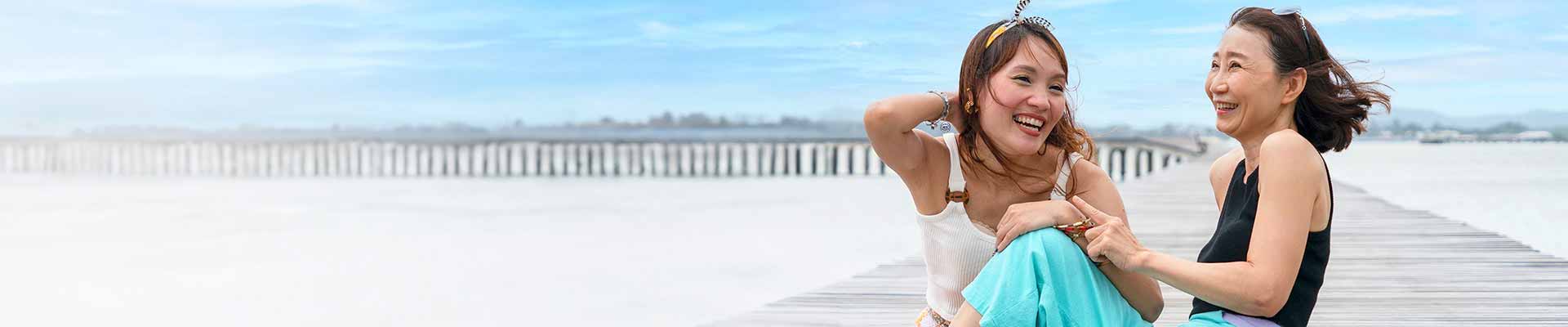 Deux femmes assises sur une jetée en bois, rient et profitent de la compagnie de l'autre par une journée ensoleillée.
