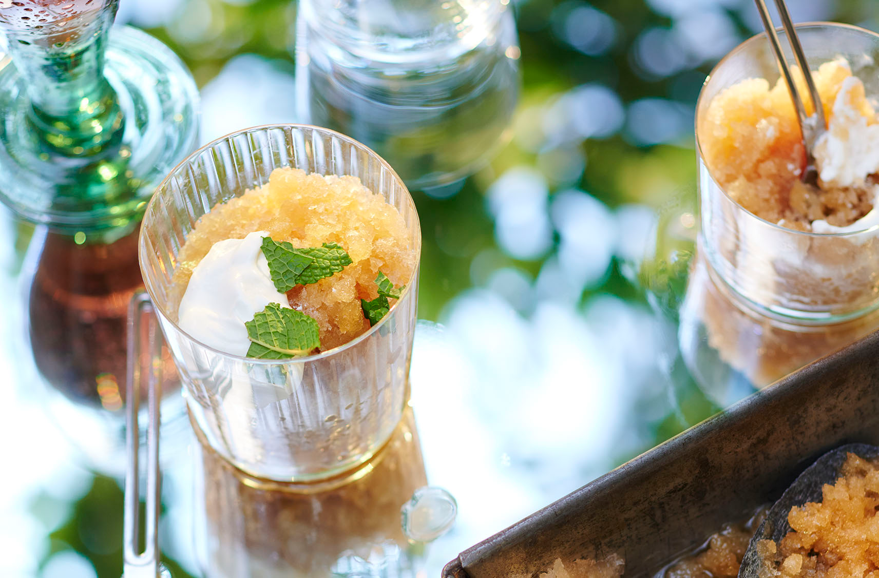 Deux verres de granité au café infusé à froid à l'agrume yuzu garni de crème fouettée et parsemé de sucre, de croustilles de noix de coco et de feuilles de menthe fraîche sur un plateau.