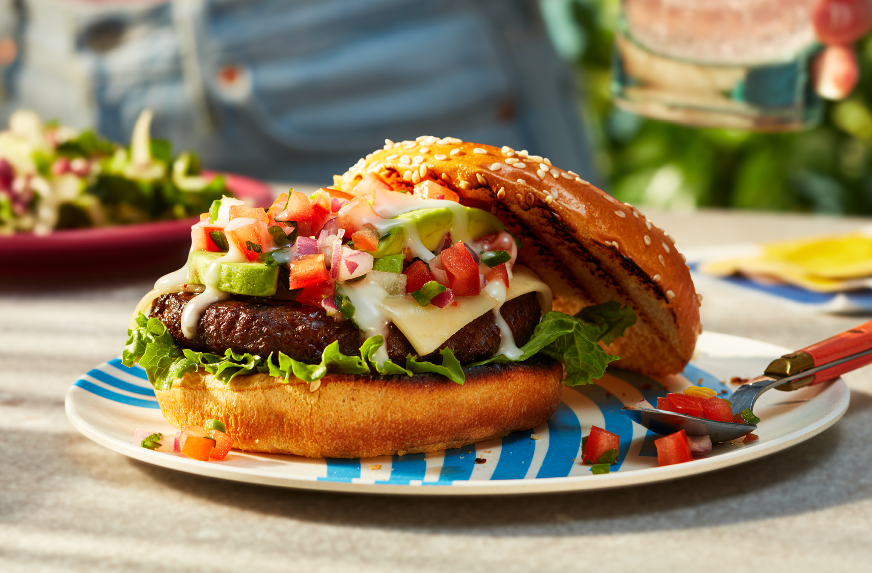 A PC World of Flavours Chipotle Beef Burger on toasted brioche buns loaded with Monterrey Jack cheese, jalapenos, avocado, pico de gallo and tangy PC Cilantro Lime Crema.