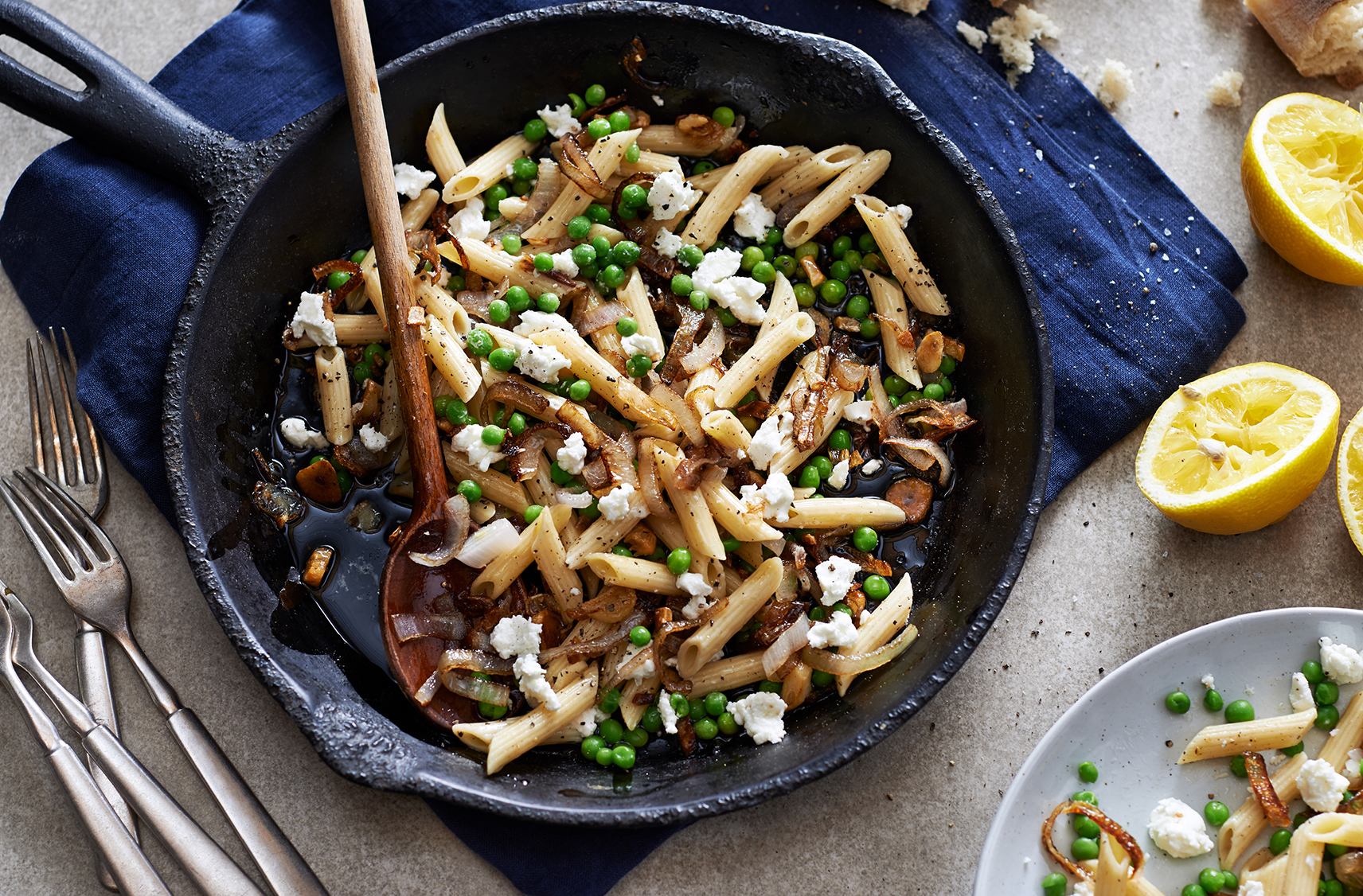 penne with peas , goat cheese and fresh herbs being served up in a cast iron skillet and a wooden spoon 