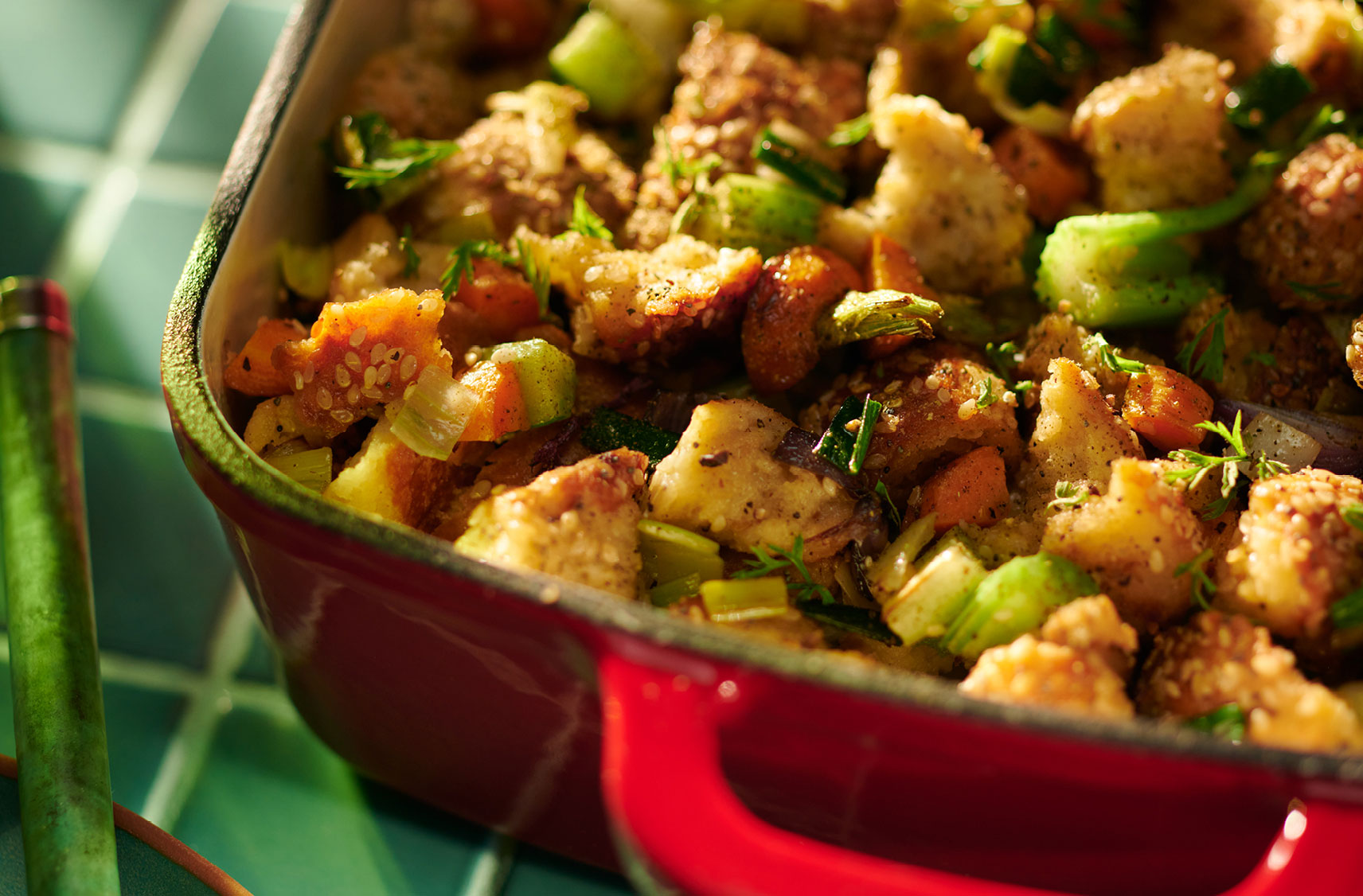A ceramic baking dish filled with a freshly baked stuffing filled with chunks of vegetables and bread pieces.