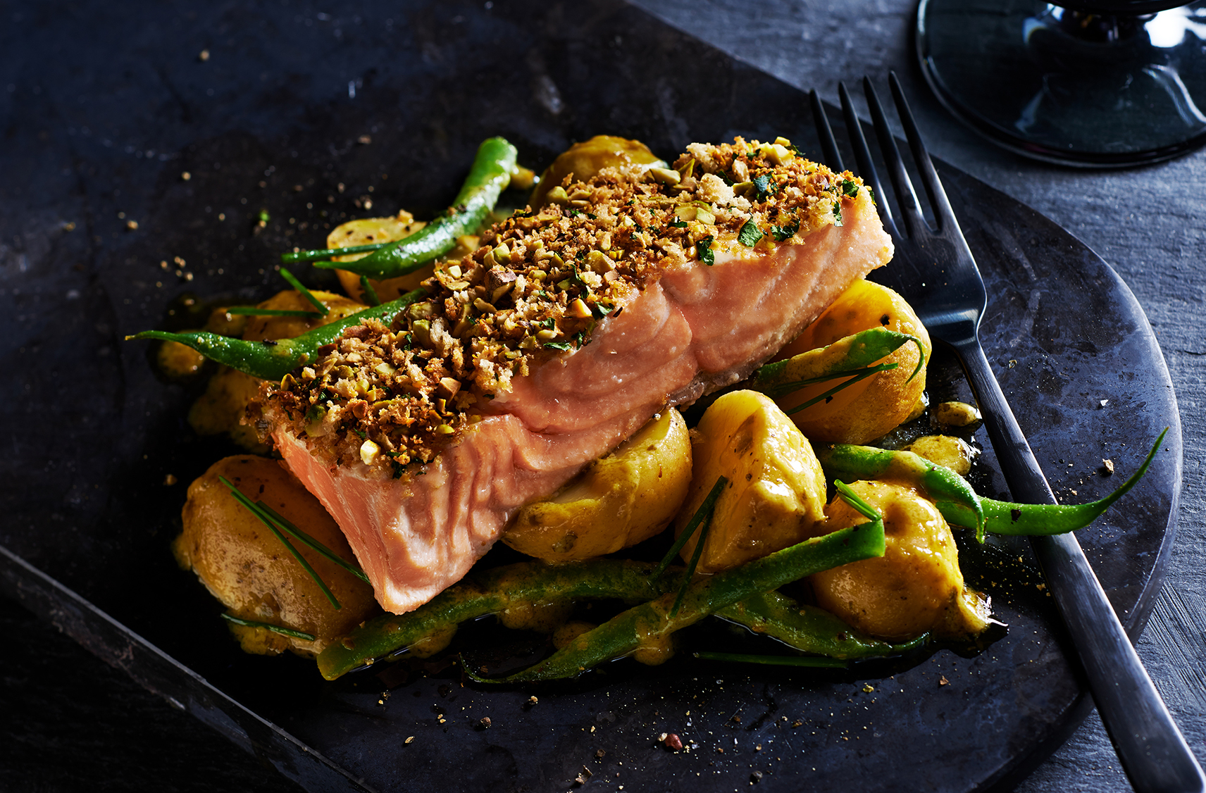 A pistachio-crusted salmon fillet on top of mini potatoes & green beans