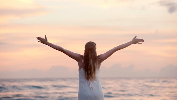 Woman With Arms Raised at Beach During Sunset