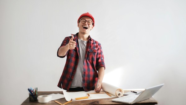 Laughing male constructor showing thumb up at a working desk