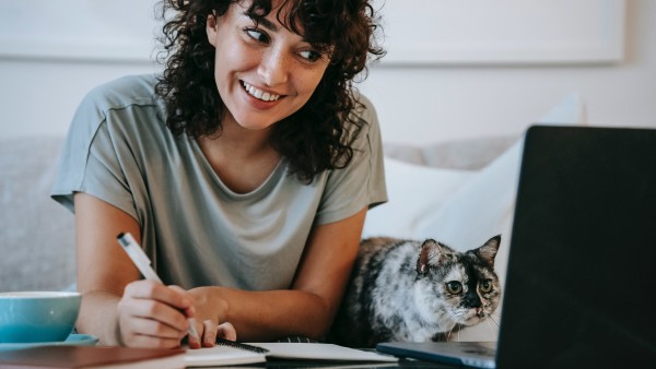 Woman with a cat writing in a planner while using laptop