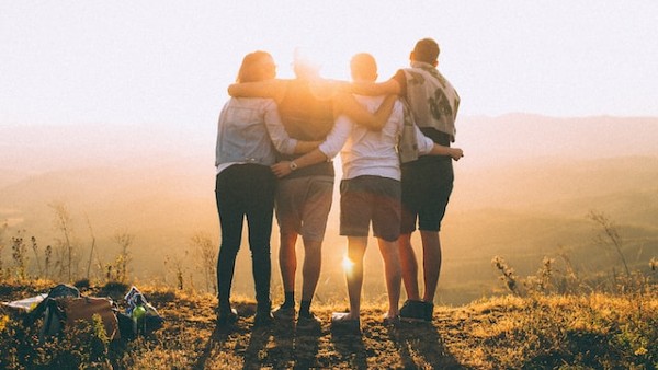 four person hands wrap around shoulders while looking at sunset
