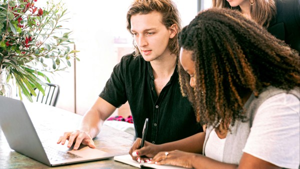 Man working on laptop while a woman takes notes