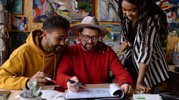 Men and Woman Discussing Project in a Sketchbook and Abstract Paintings Hanging on a Wall
