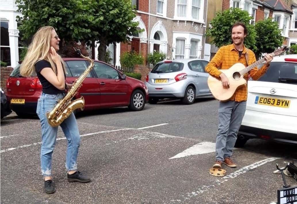 Chloe Edwards-Wood from Give a Song playing sax in street with guitarist