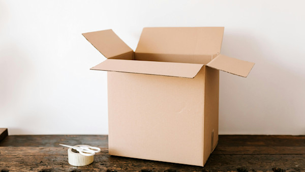 Cardboard box on dark wooden table near tape and scissors