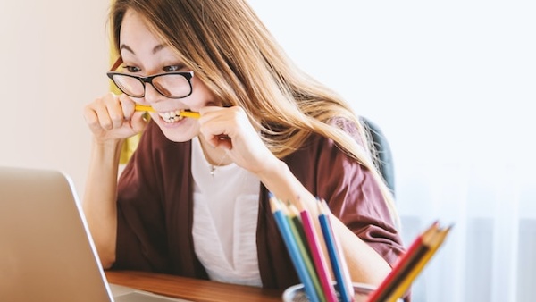 woman biting pencil while sitting on chair in front of computer during daytime