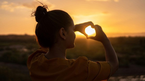 Woman doing a hand heart sign to the sun