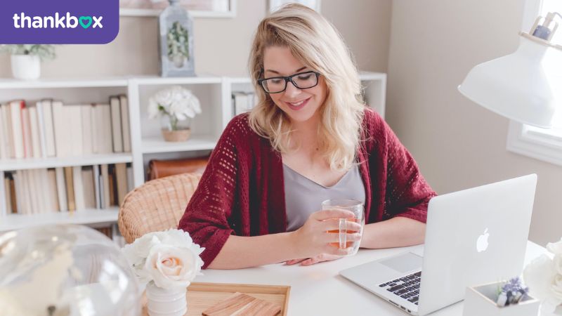 work life balance woman smiling holding glass mug sitting beside table with MacBook