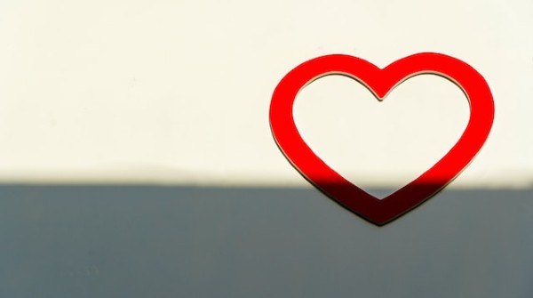 A red heart, partially in shadow on a white background, looking like it is rising from the shadow, into the light.