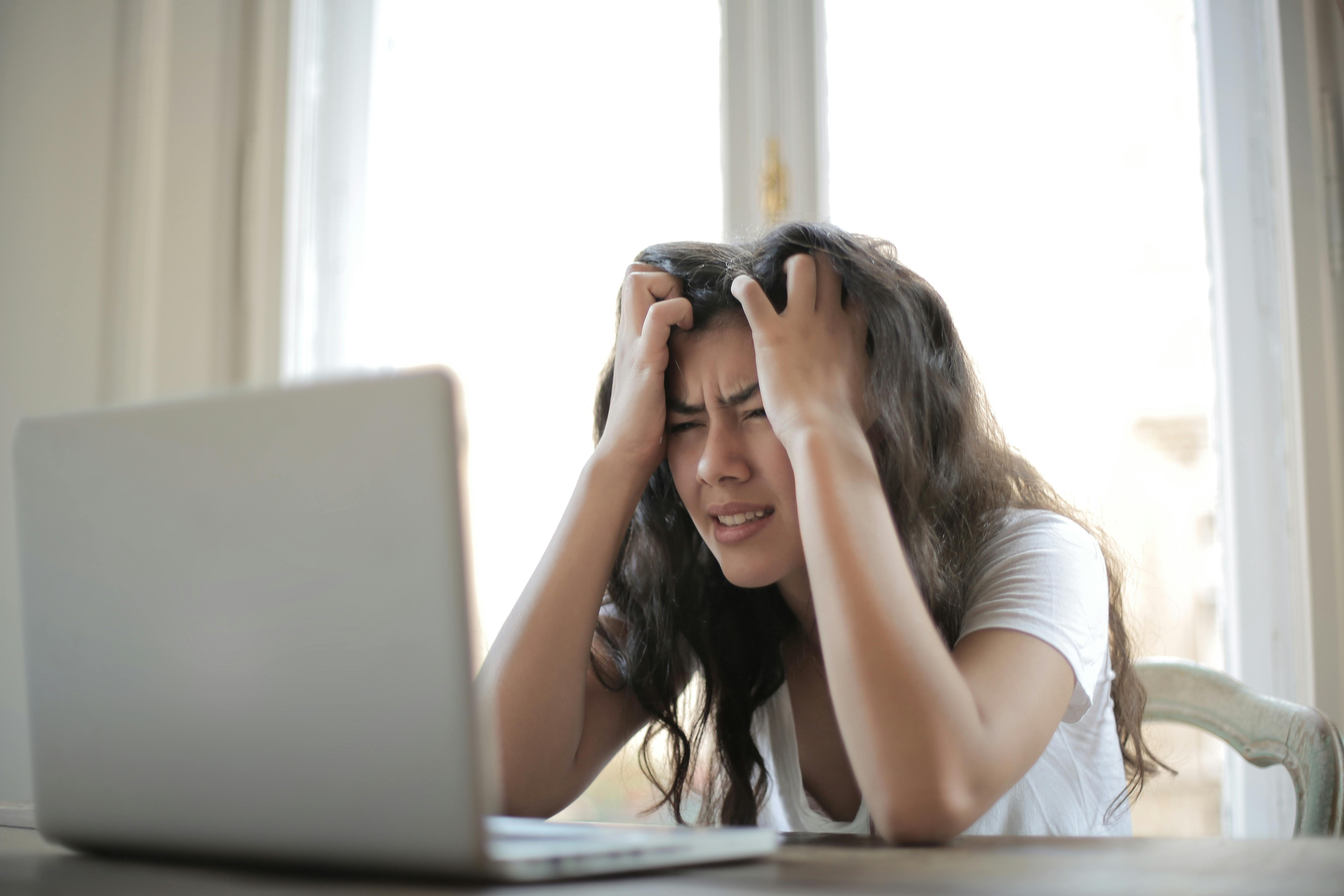 Woman in a white shirt sits at her desk, frustrated with her head in her hands