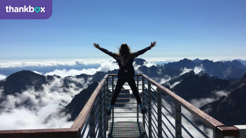 Woman Standing on Handrails With Arms Wide Open Facing the Mountains and Clouds
