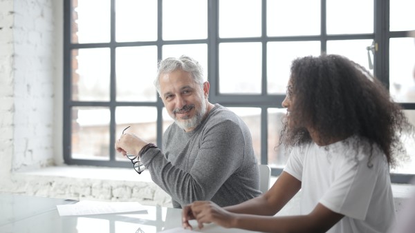 Cheerful senior mentor supporting young colleague in office