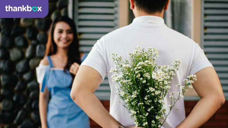 Man holding a bouquet behind his back while a woman is standing in front of him