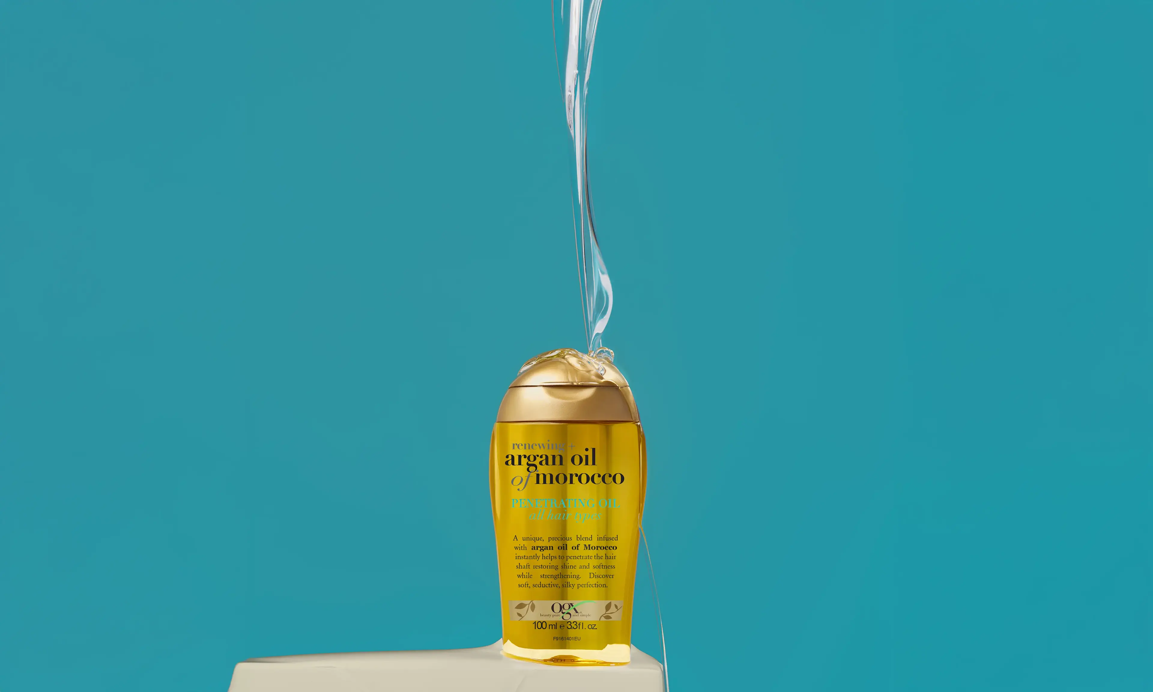 OGX® Argan Oil of Morocco Penetrating Oil being poured over a bottle of Penetrating Oil.