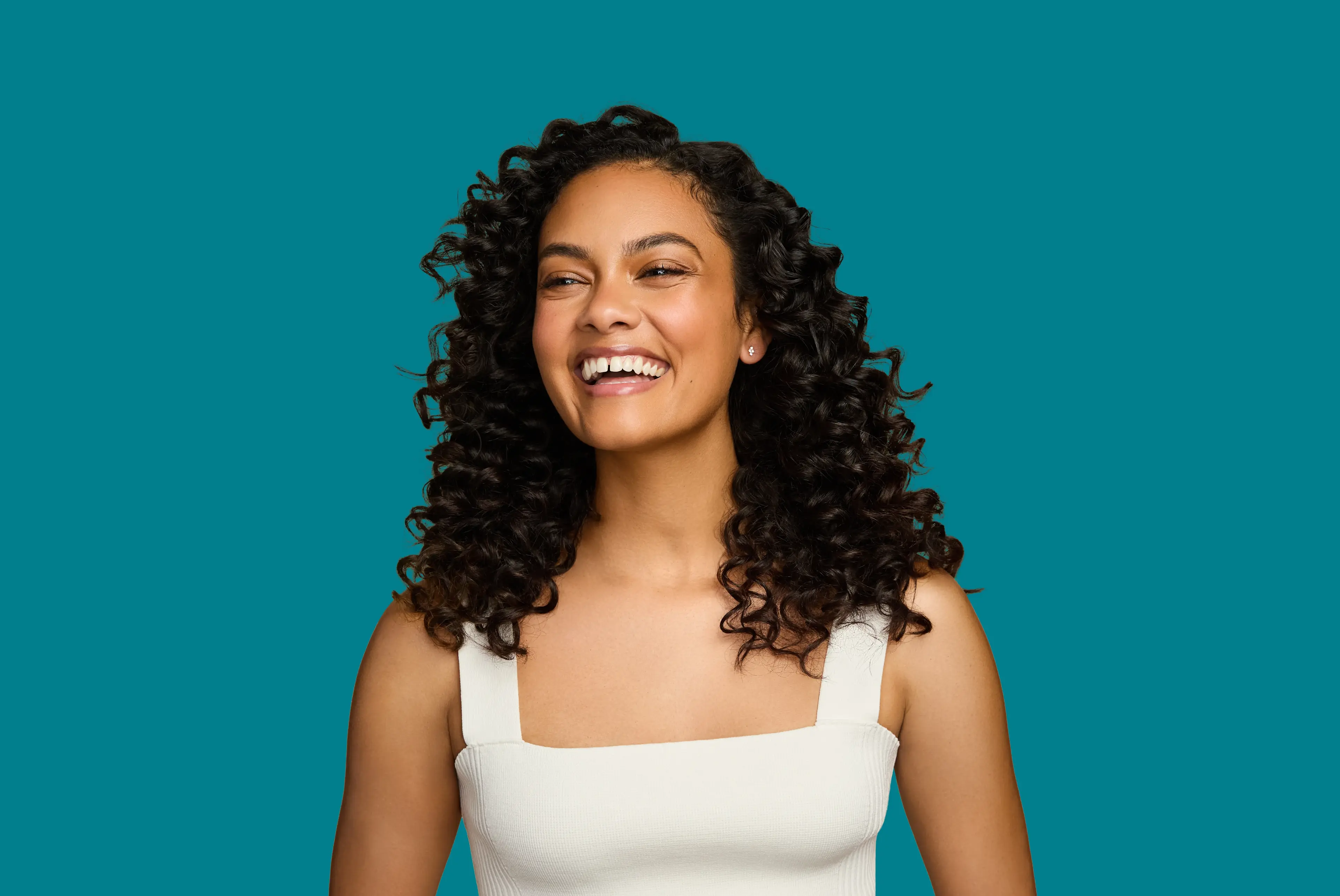 Smiling woman with healthy curls after using OGX® Beauty products