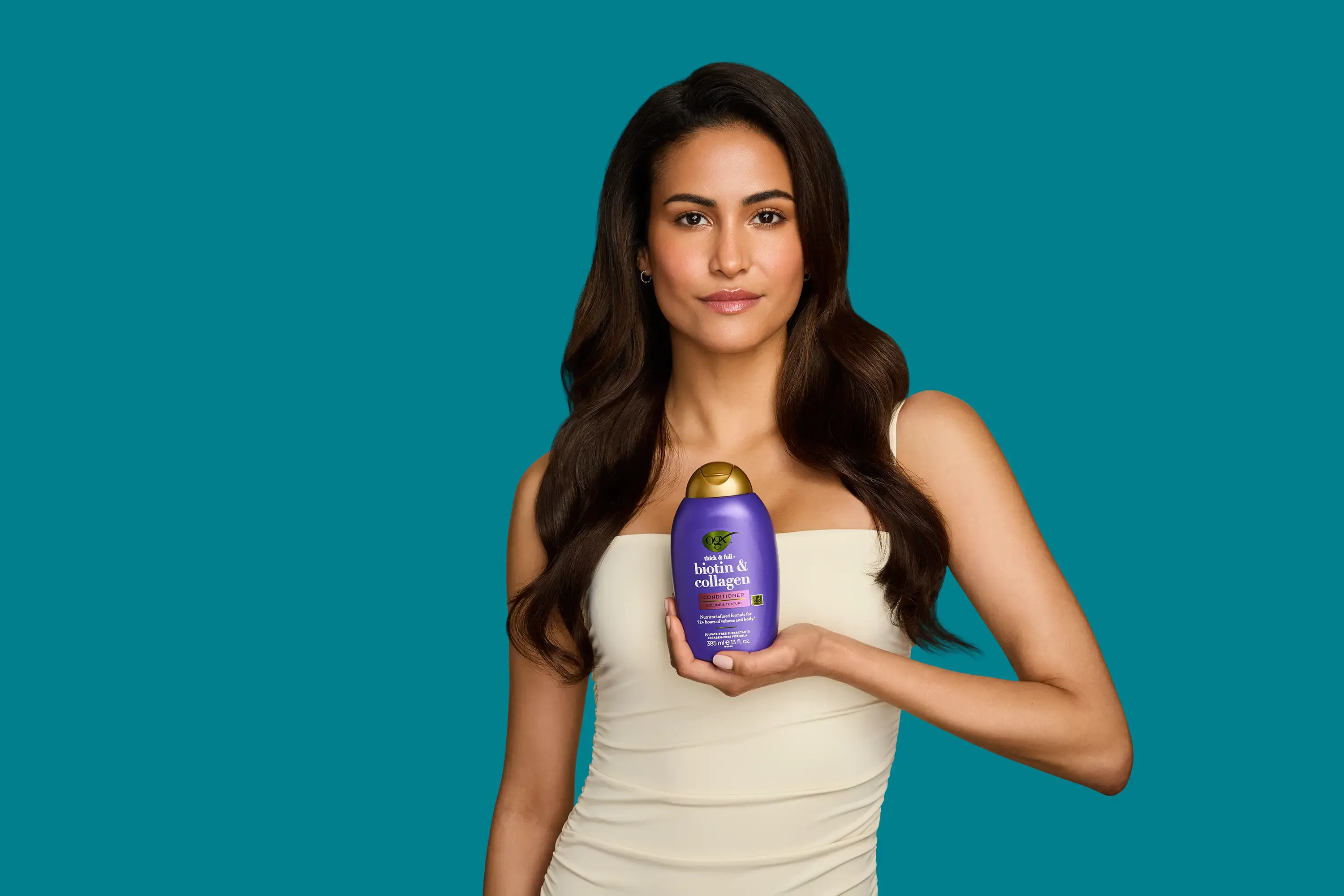 Woman with shiny healthy hair holding OGX® Biotin & Collagen conditioner