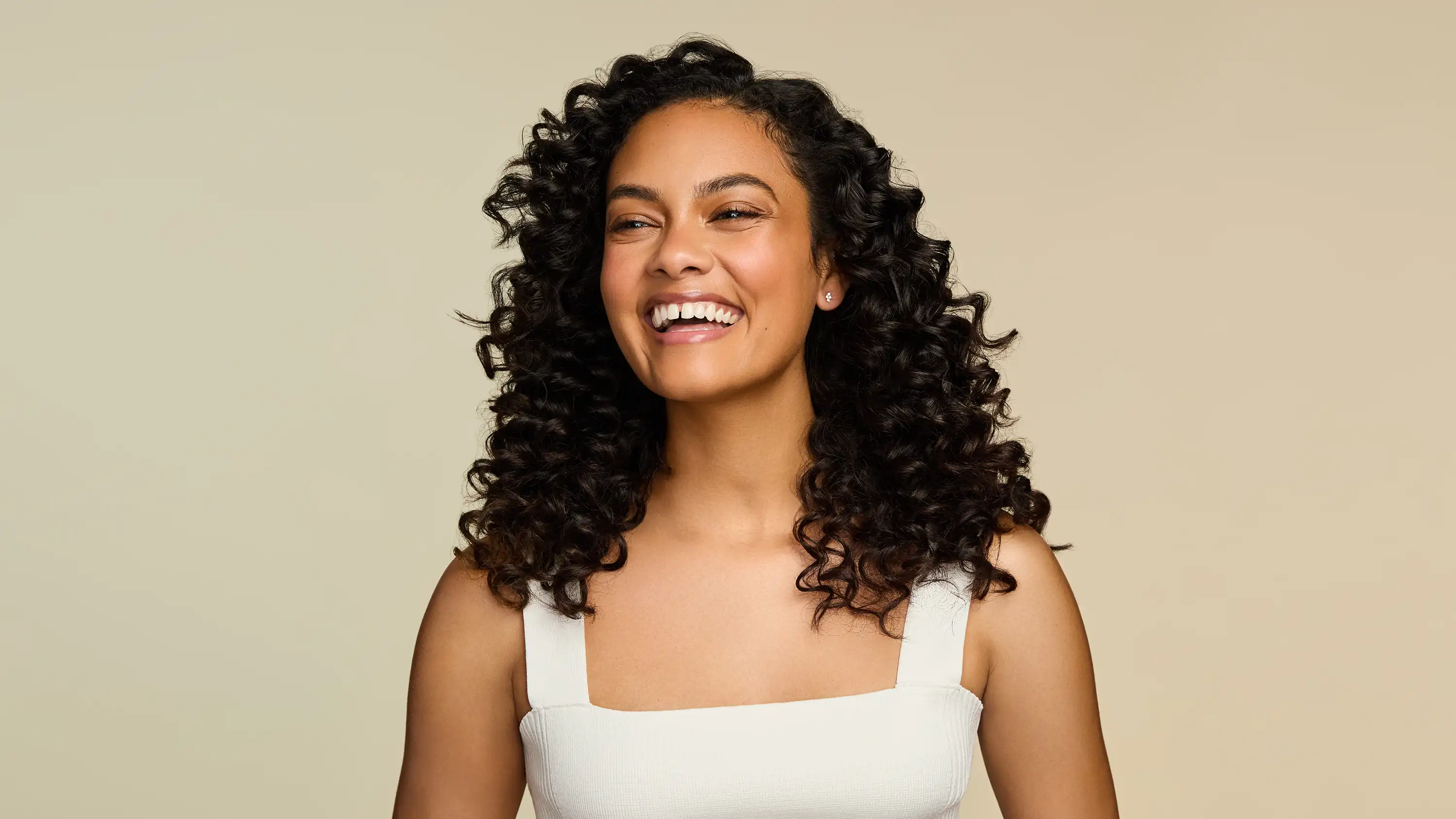Smiling woman with healthy curls after using OGX® Beauty products