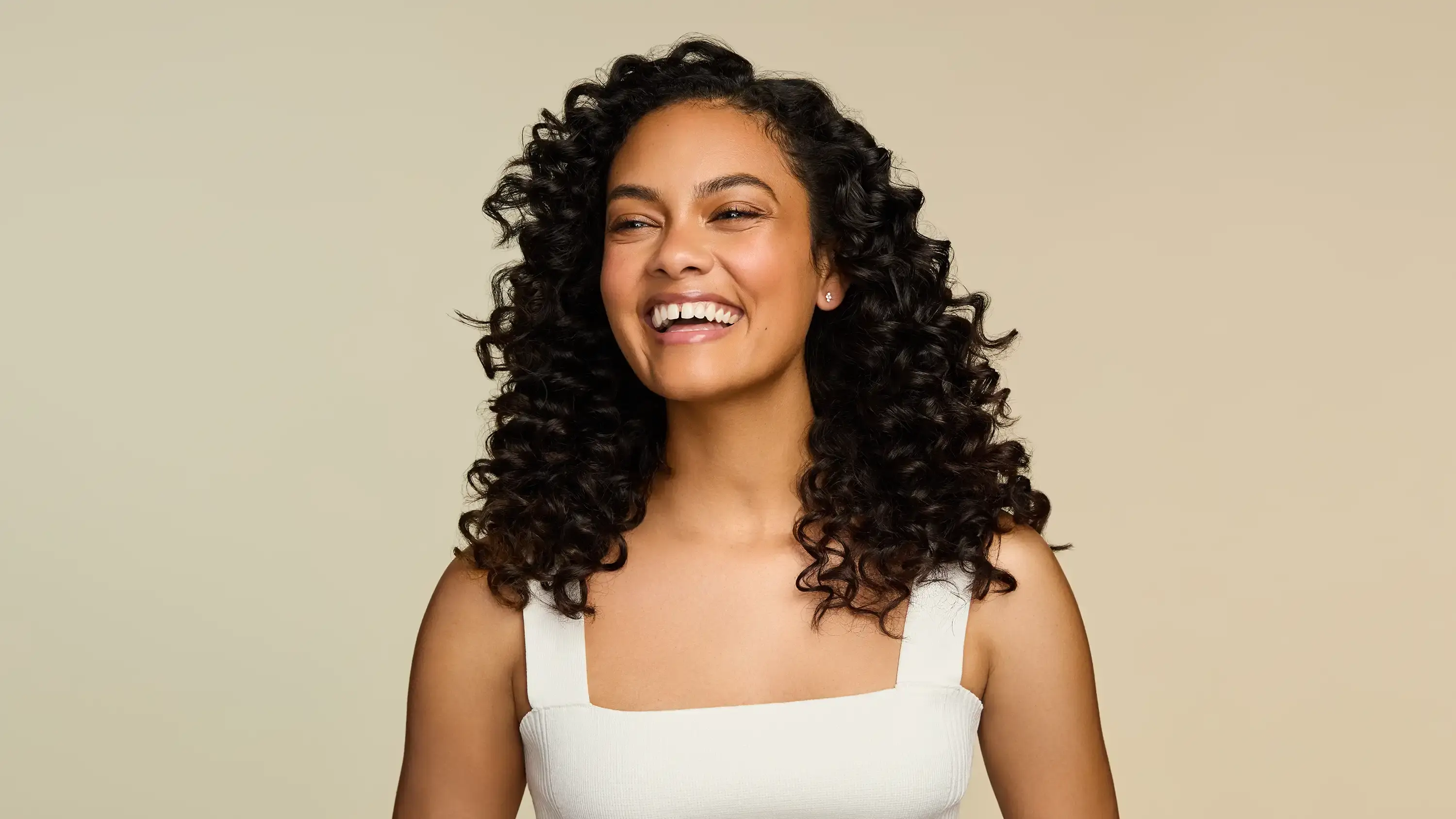 Smiling woman with healthy curls after using OGX® Beauty products