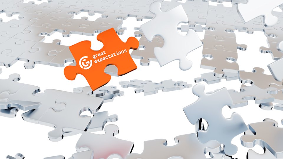 silver puzzle pieces partially assembled and partially piled, with a single orange piece that has the GX logo on it in focus