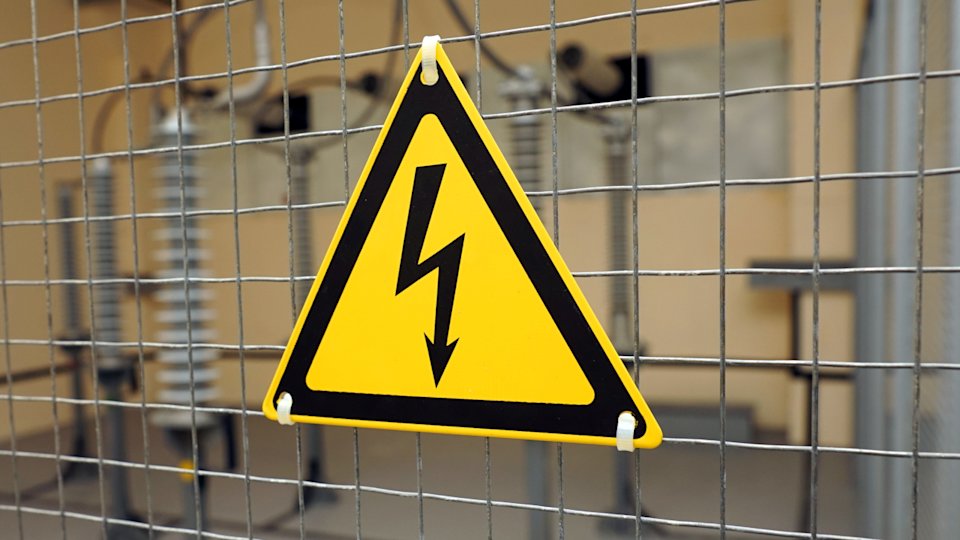a photo of a triangular electrical hazard warning sign zip tied to a metal grid