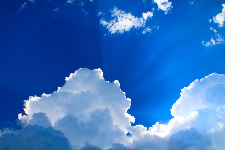 A photo of white cumulus clouds backlit against a bright blue sky