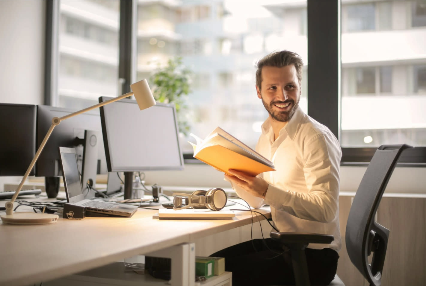 smiling man working at a desk with computer and book