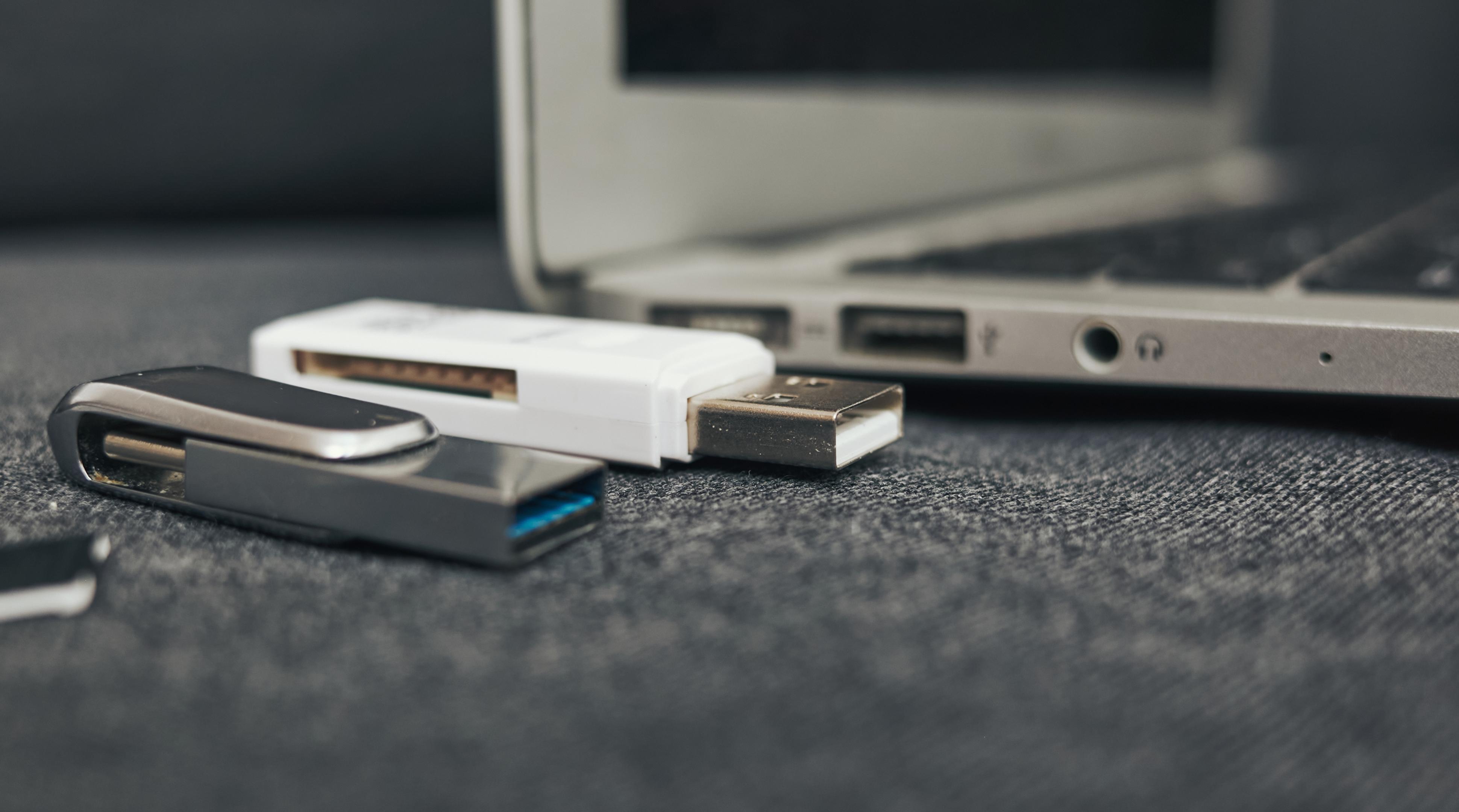 Laptop with a white USB drive and a black USB drive on top of it. The laptop is open and the USB drives are attached to it