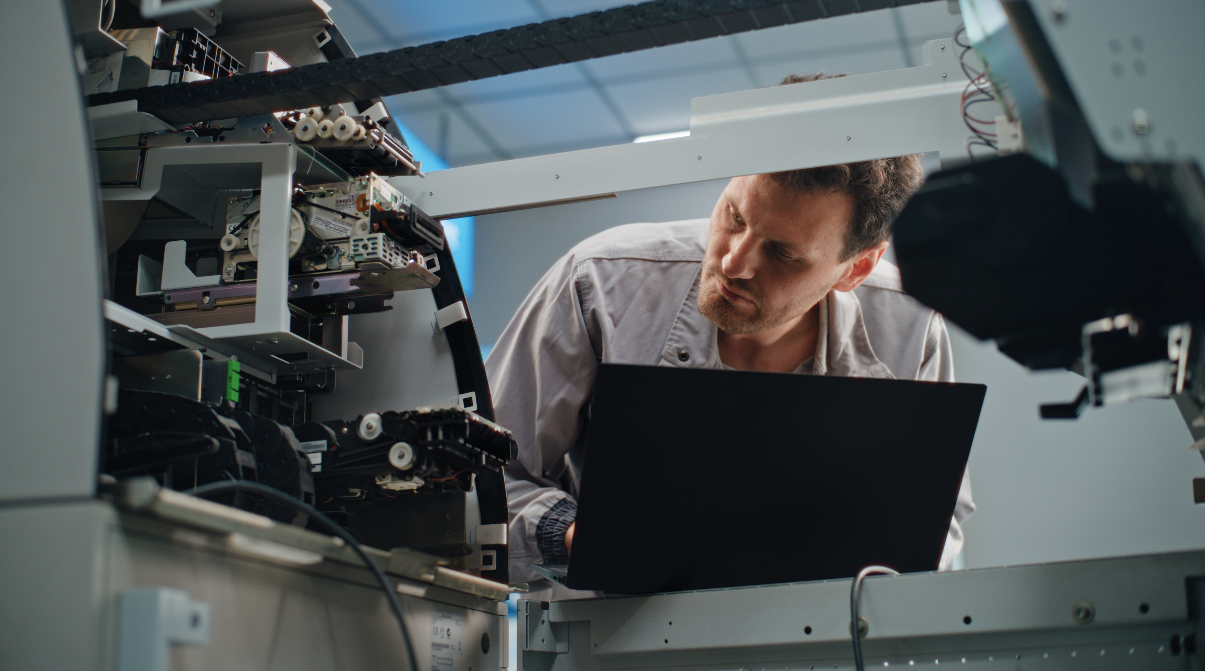 ATM Technician in Uniform Servicing Cash Dispenser Machine in Modern Airport Terminal. Male Worker Setting ATM Machine Using Laptop Computer. Banking Technology, Cash Withdrawal Systems and ATM Repair