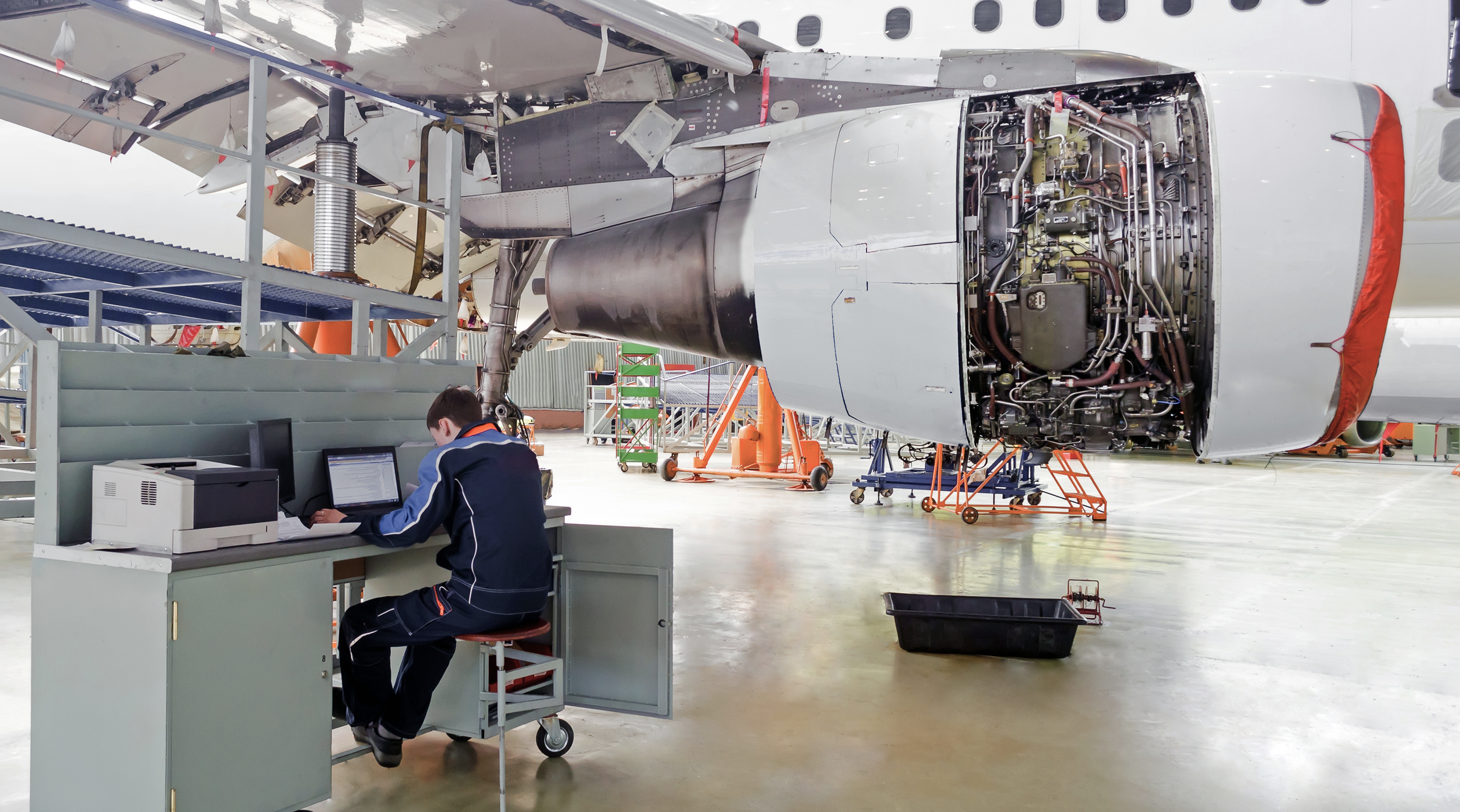 Aircraft service, diagnostics, inspection, repair, view of the engine of the aircraft and with a technician at the computer in the air industry hangar