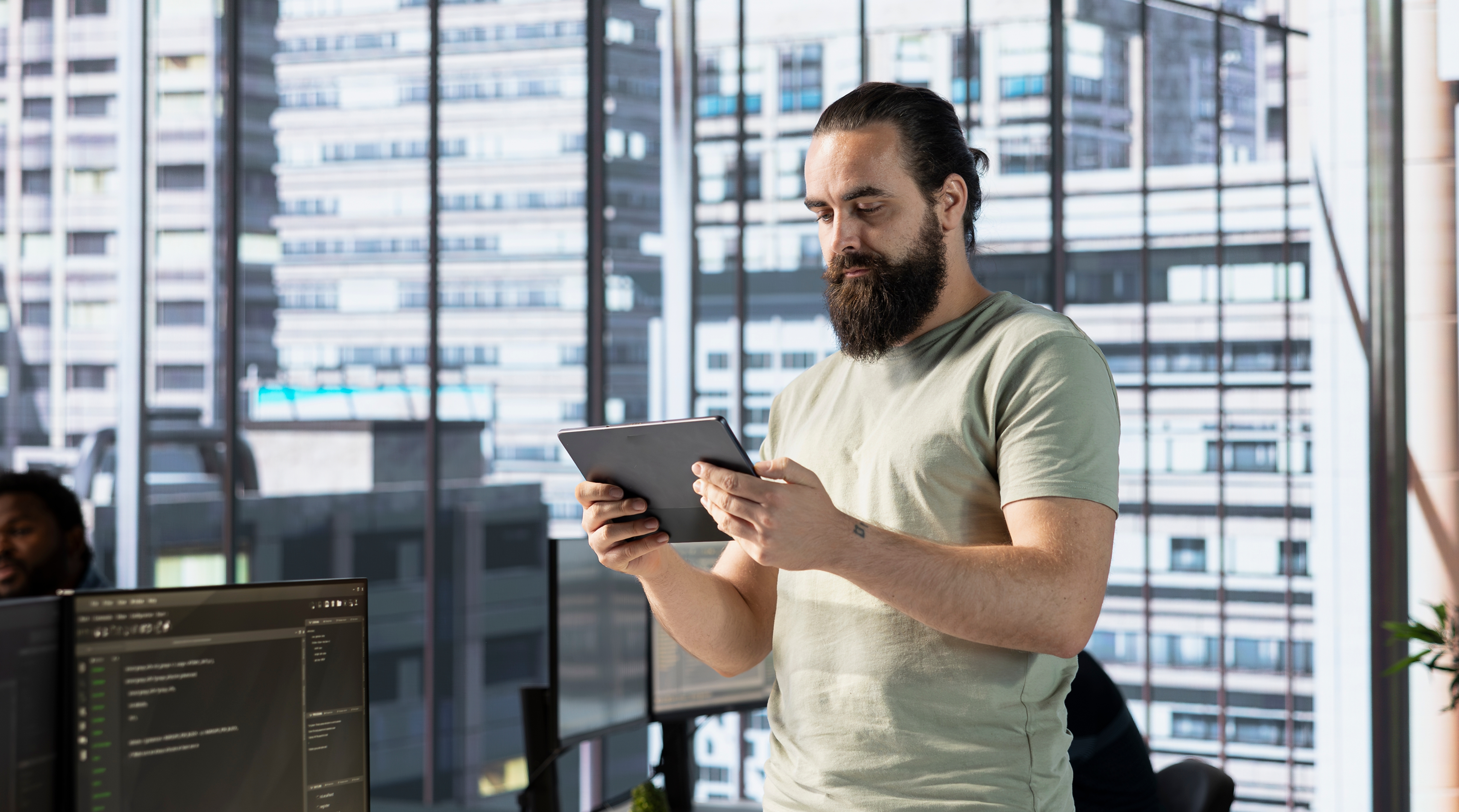 Programmer creating machine learning models that can process and analyze data to improve and automate decision making processes, looking at tablet. Man programming in office using device