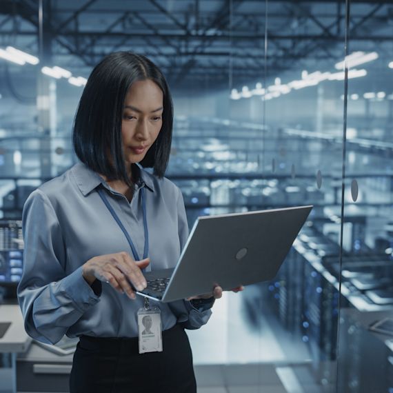 Smiling Female Data Center Specialist Analyzes Server Performance on a Laptop.