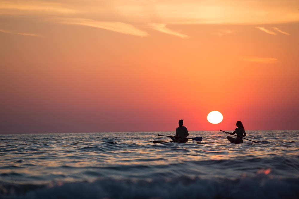 Man and woman paddleboarding during sunset