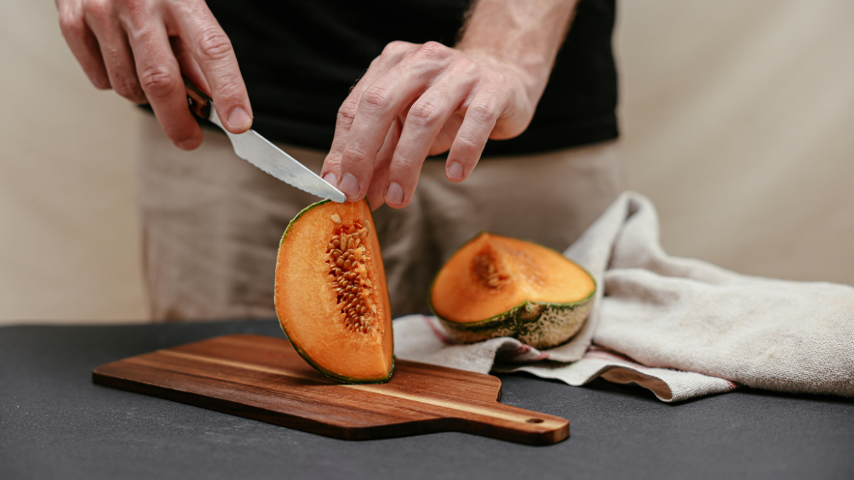 Man slicing fresh rockmelon on a wooden chopping board as a whole-food snack
