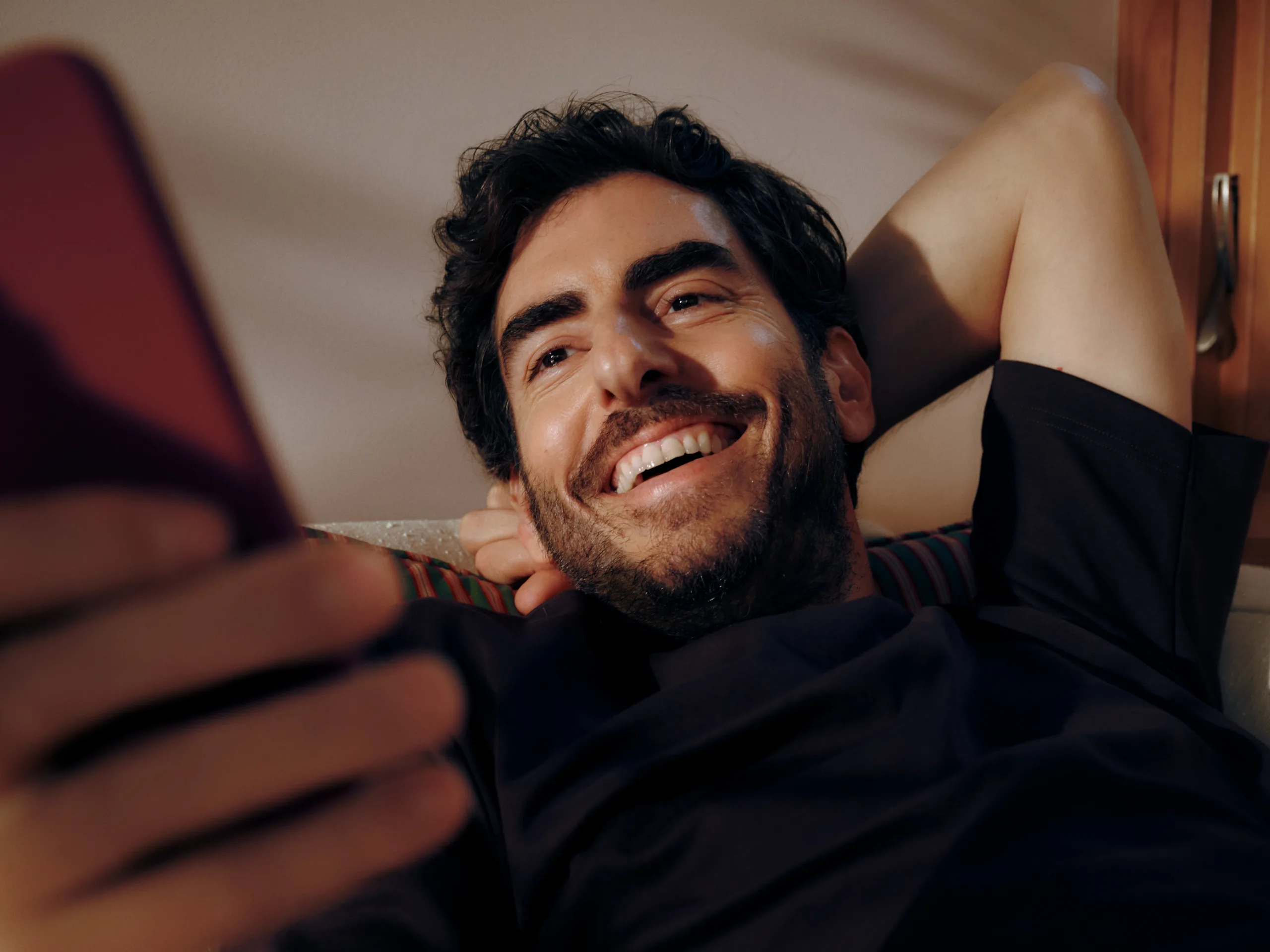 Man sitting on his couch looking happily at his phone