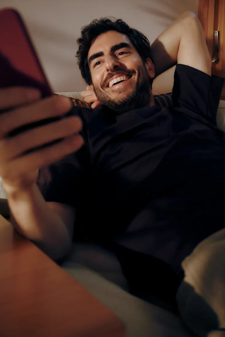 Man sitting on his couch looking happily at his phone