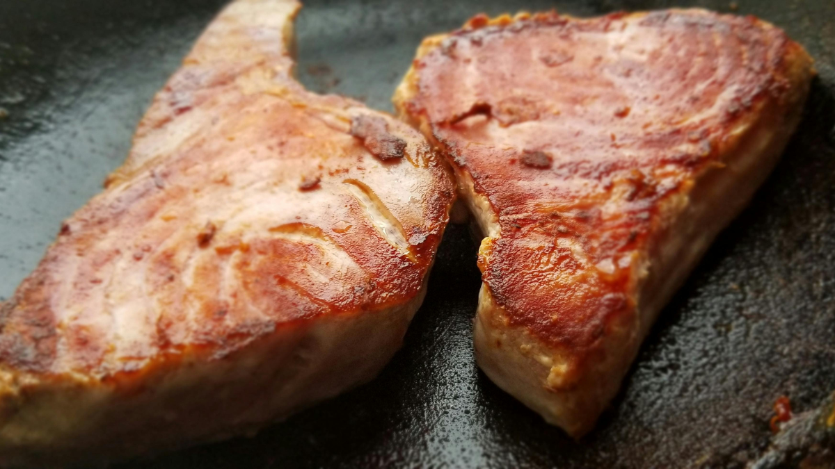 Two tuna steaks searing in a pan, a source of protein and healthy omega-3 fats