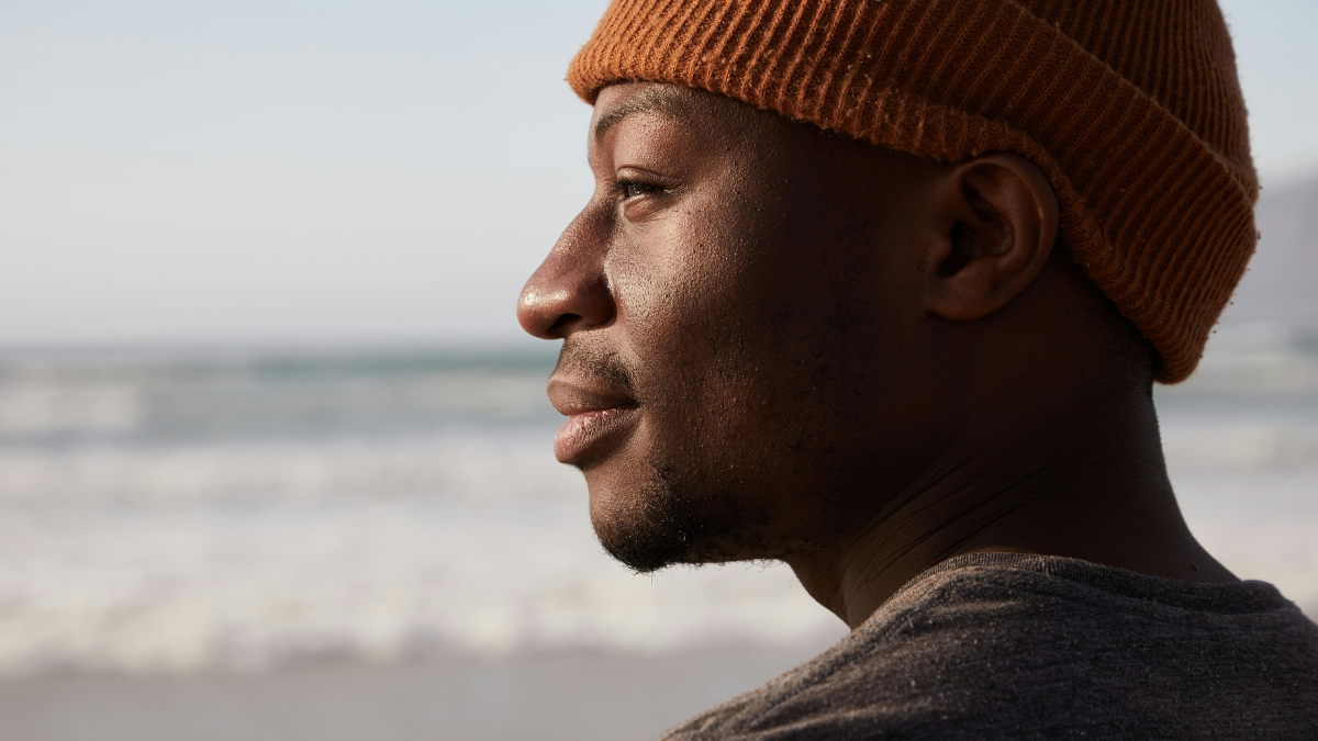 Man in a beanie looking out over the ocean, reflecting on building lasting healthy habits